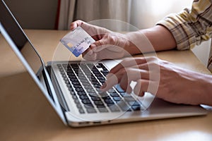 Selective focus shot at credit card mock up. Asian men hand holding credit card while type information into computer laptop device