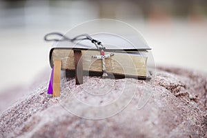 Selective focus shot of a cross placed on an old bible captured on a rock-concept: Christianity