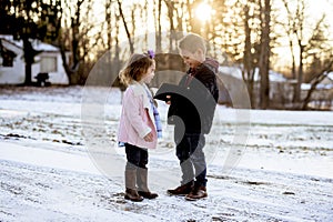 Selective focus shot of cute little kids reading the Bible in the middle of a winter park