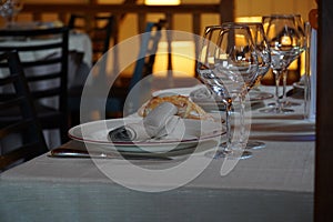 Selective focus shot of eating utensils and a wine glass arranged in a dining table of a restaurant