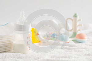 Selective focus shot of a feeding bottle, baby rattle, pacifier, rubber duck and disposable towels