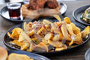 Selective focus shot of French fries with melted cheese and sliced sausage on a wooden table