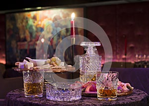 Selective focus shot of a glass of whiskey and a crystal wine bottle on a table