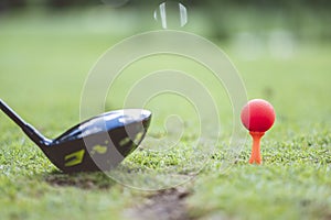 Selective focus shot of a golf club and red golf ball on the grass-covered golf course