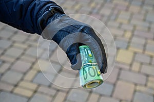 Selective focus shot of a hand wearing a leather glove holding a roll of euro banknotes