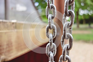 Selective focus shot of the metal chains of a swing set with the trees in the background