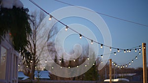 Selective focus shot of outdoor string lights hanging on line on outside house in backyard in cozy evening winter on