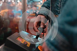 Selective focus shot of a person playing a claw crane machine game in an arcade