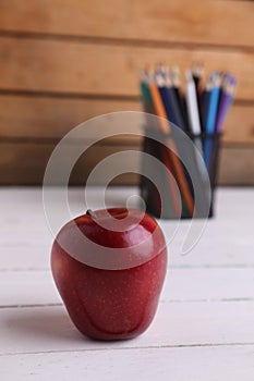 Selective focus shot of a red apple with colored pencils in a pencil holder