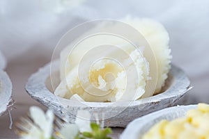 Selective focus shot of shea butter in a saucer and some white flowers on a white table top