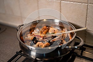 Selective focus shot of shrimps and clams being cooked in gravy in a pot on a stove