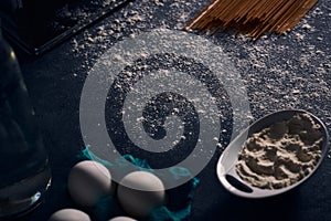 Selective focus shot of a sprinkled flour with a white bowl, eggs, and uncooked pasta