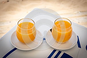 Selective focus shot of two orange juice glasses in white plate on a table
