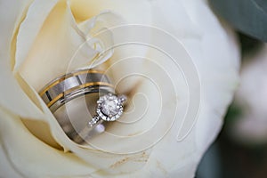 Selective focus shot of wedding and engagement rings in between the petals of a white rose flower