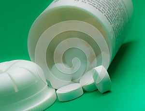 Selective focus shot of white round pills pouring out of the medicine bottle on green background