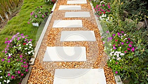 Selective focus shot of white stone path with yellow and brown gravel in colorful flower garden and green grass shows beautiful