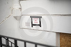 Selective focus shot of a white wall with a sign 'caution wet floor'