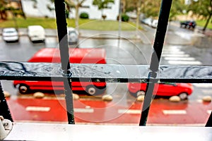 Selective focus shot through  the window bars of two red vehicles parked on street on a rainy day