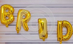 A selective focus shot of the word `bride` made of golden balloons on a wall.