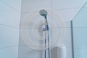 Selective focus on shower in clean public hospital bathroom. White tiles on walls with glass septum. Closeup.