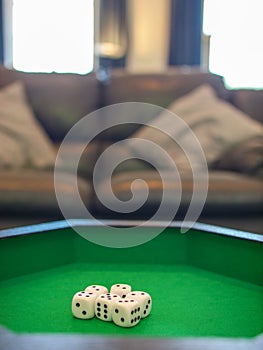 Selective focus of six dice in a green carpeted tray in a living room with a sofa in the background