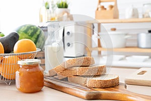 Selective focus on sliced whole wheat bread on wooden tray with apricot jam in jar, bottle of fresh milk, oranges, avocado