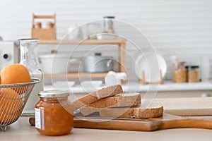 Selective focus on sliced whole wheat bread on wooden tray with apricot jam in jar, bottle of fresh milk, oranges in basket