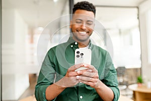 Selective focus on the smartphone in hands of happy and cheerful indian man, male office employee using phone, scrolling