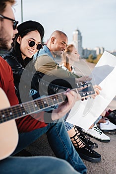 selective focus of smiling multiethnic friends with map and guitar