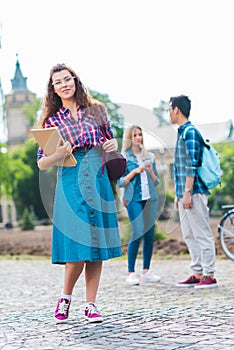 selective focus of smiling student with notebook and multicultural classmates behind