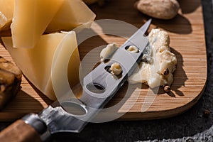 Selective focus of soft dorblu pressed by knife next to pieces of grana padano on cutting board.