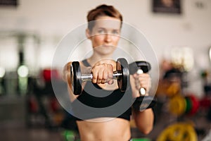 Selective focus of sporty woman with dumbbell weights in gym.