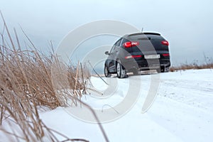 Selective focus. SUV car racing on snowy road in countryside during winter travel. Track of vehicle in snow