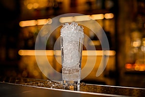 selective focus on tall glass full of ice pieces on bar counter