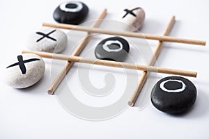 Selective focus of tic tac toe game with grid made of paper tubes, and pebbles marked with naughts and crosses