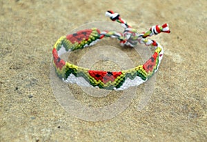 Selective focus of tied woven friendship bracelet with watermelon pattern handmade of thread on beige stone