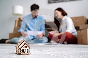 Selective focus on tiny toy house and blurred background with couple on floor