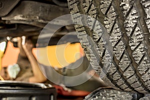 Selective Focus on a tire of an SUV elevated on jack stands at a garage a mechanic is visibly working on the underchassis