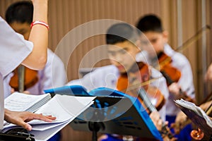 Selective focus to hands of conductor with music notation. hands of  conductor with blurry Asian boy students playing violin