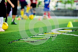 Selective focus to ladder drills on green artificial turf with blurry coach and kid soccer are training