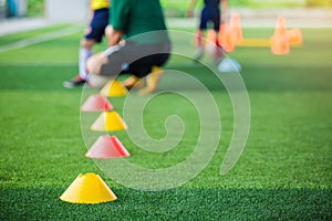 Selective focus to marker cones are soccer training equipment on green artificial turf with blurry coach is training kid players b