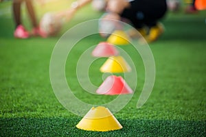 Selective focus to marker cones are soccer training equipment on green artificial turf with blurry coach is training kid players b