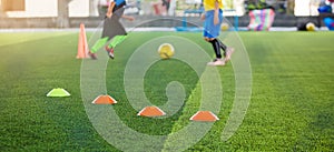 Selective focus to marker cones are soccer training equipment on green artificial turf with blurry kid players training background