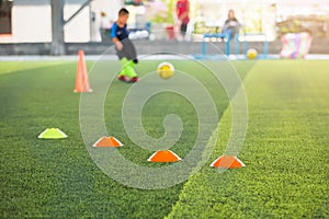 Selective focus to marker cones are soccer training equipment on green artificial turf with blurry kid players training background