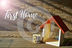 Selective focus of toy house and people miniatures with text FIRST HOME
