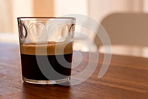 Selective focus of transparent glass of espresso with froth placed on wooden table. photo