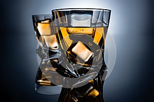 selective focus of two glasses of cognac with ice cubes, on dark