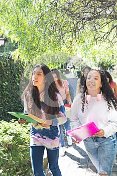 Selective focus of two teenage latinx friends happily going to high school with other friends behind them on a sunny morning photo