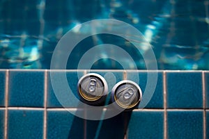 Selective focus Two white beer cans are placed at the edge of the pool with space for text input. The water surface in the blue