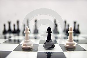 Selective focus on two white and one black pawn chess piece on a chessboard set.